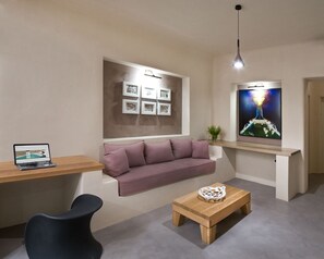 Una sala de estar moderna con un sofá, una mesa de centro, un escritorio con una laptop, un televisor montado en la pared y cuadros enmarcados.