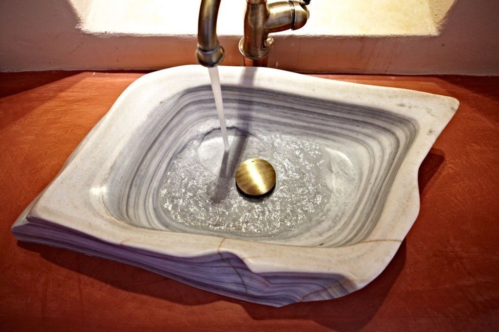 Un lavabo de cerámica cuadrada con un objeto dorado en el centro, un grifo encima y una encimera marrón.