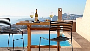 Una mesa con dos sillas, una botella de vino y copas en una terraza con vista a una piscina y al mar.