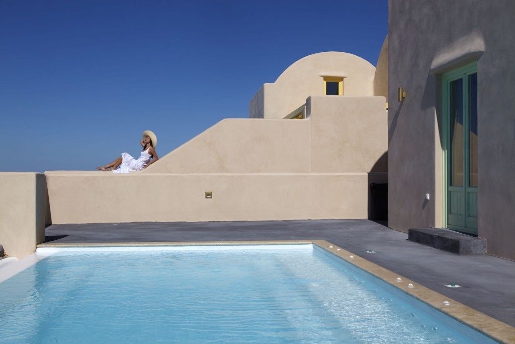 A pool area with a person sitting on a ledge, a building with a curved facade, and a door with a green frame.