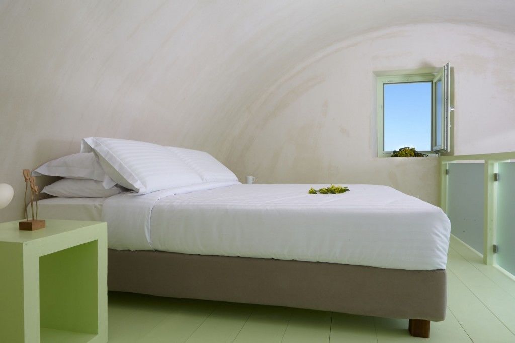 A bedroom with a bed, a bedside table, a small window, and a green wall.