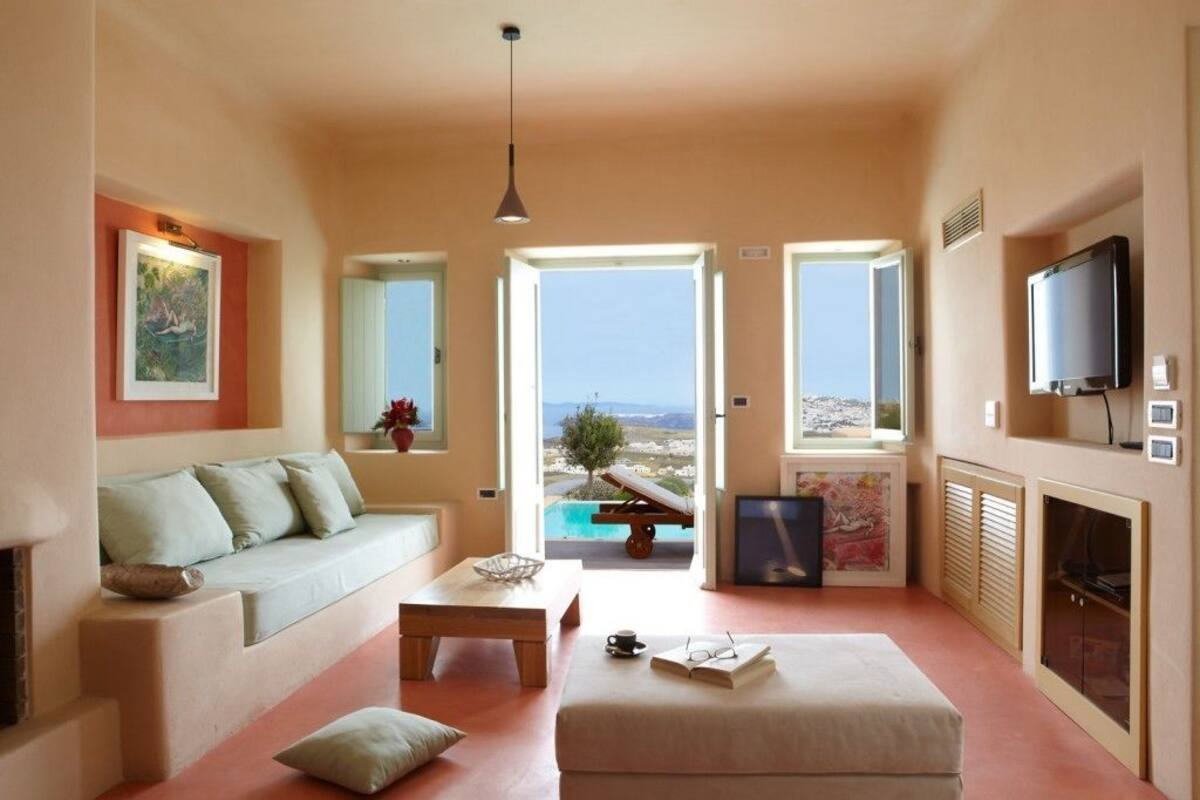 Ein geräumiges Wohnzimmer mit einer Couch, einem Couchtisch und einem Hocker. An der Wand hängt ein Fernseher und über der Couch hängt ein Gemälde.