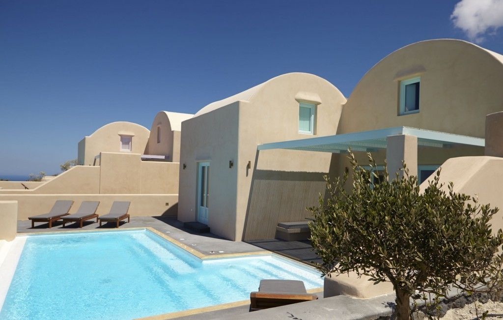 Un espace piscine avec des chaises longues, un petit arbre et un bâtiment doté d’un toit incurvé.