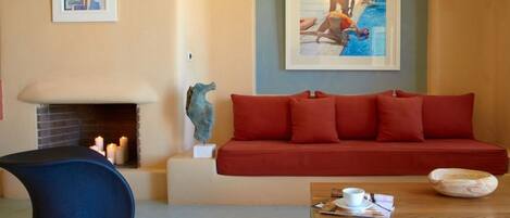 Un salon avec un canapé rouge, un fauteuil bleu, une table basse en bois et une cheminée.