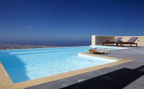 Una piscina infinita en la azotea con sillones y vistas a la costa.