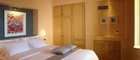 A bedroom with a bed, a wardrobe, a painting, and a window.