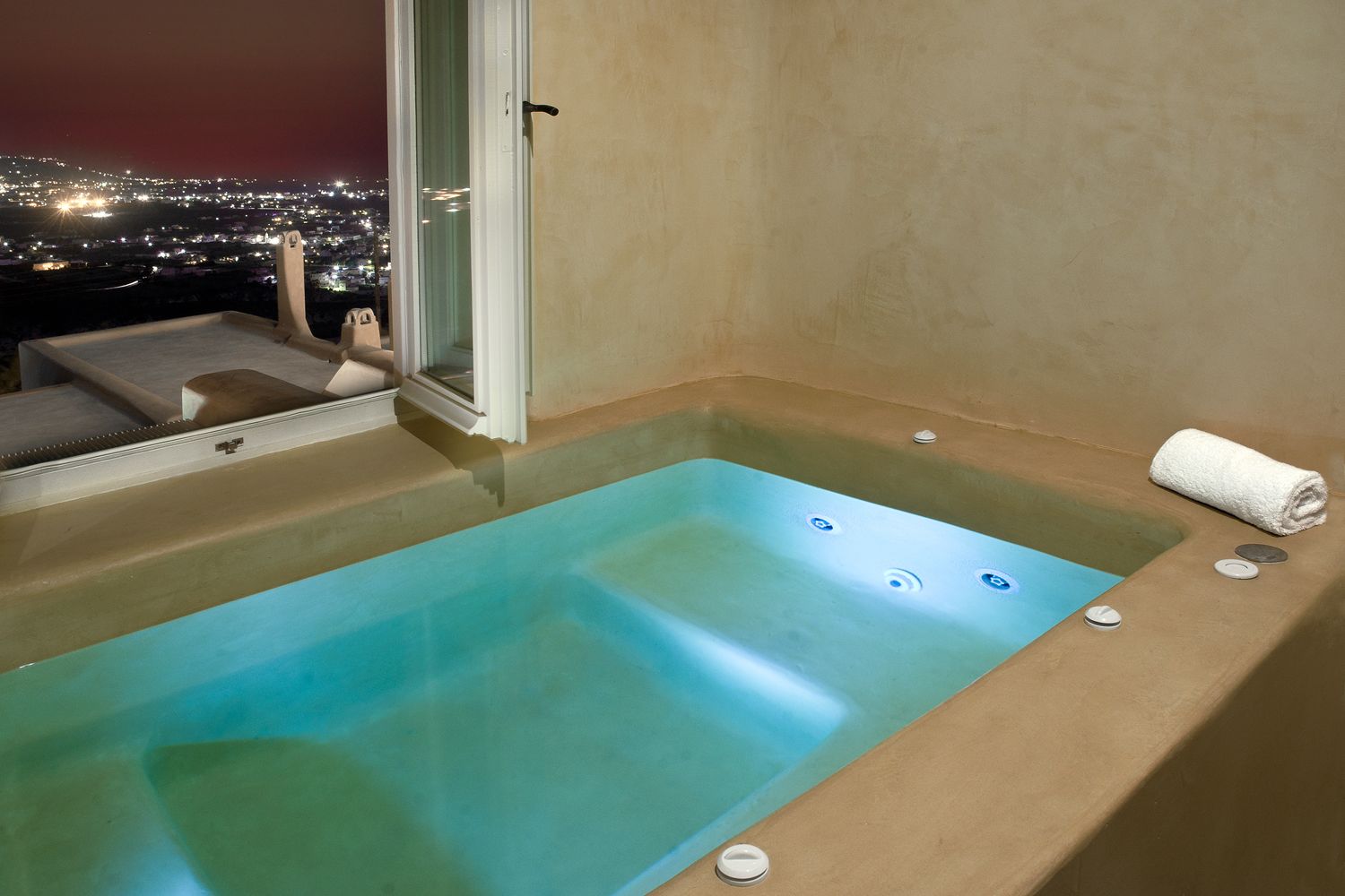A spa area with a large bathtub, a glass door, and a view of a cityscape at night.