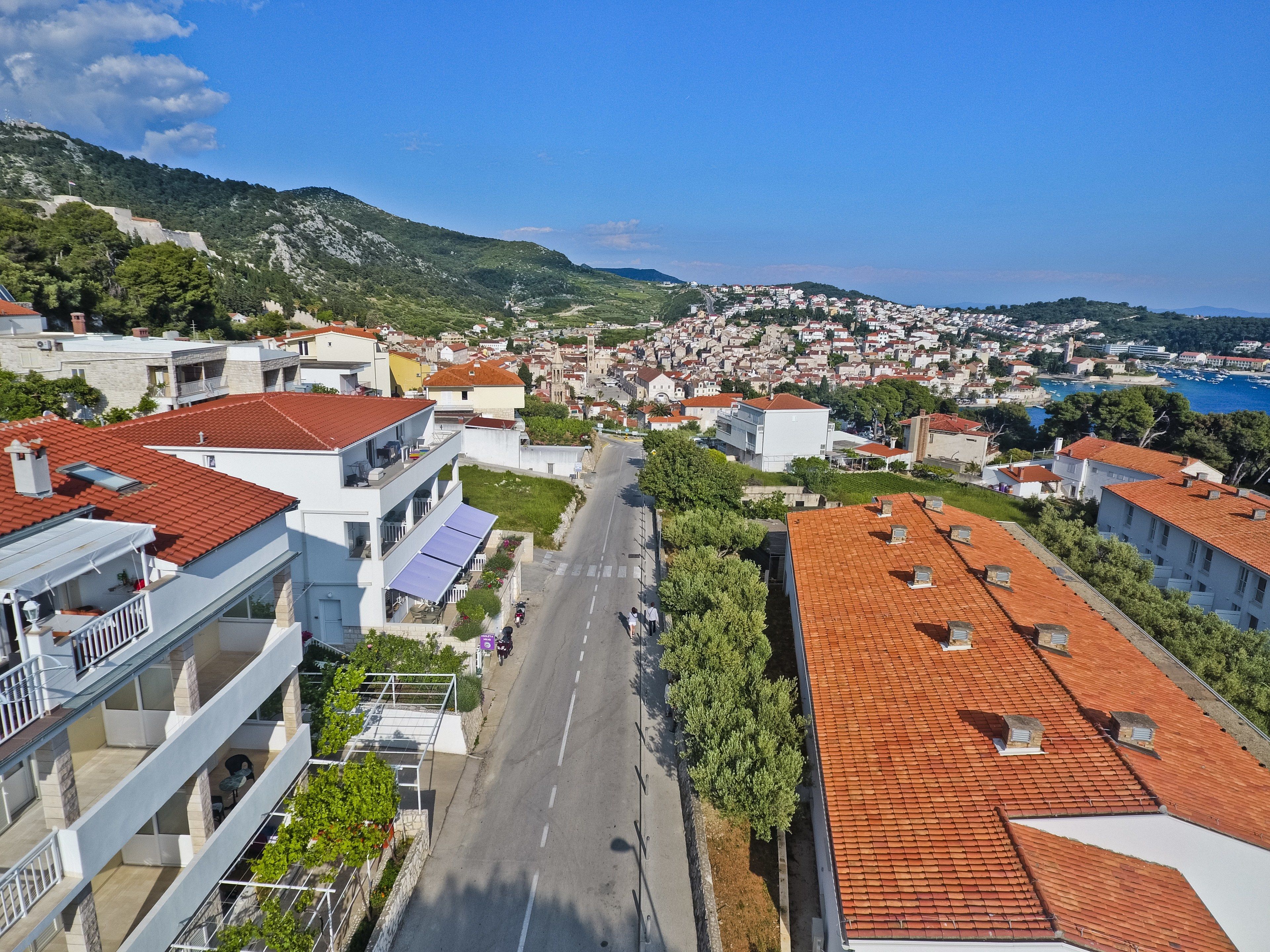 Une ville côtière aux bâtiments aux toits de tuiles rouges, avec une rue principale et une vue sur la mer.