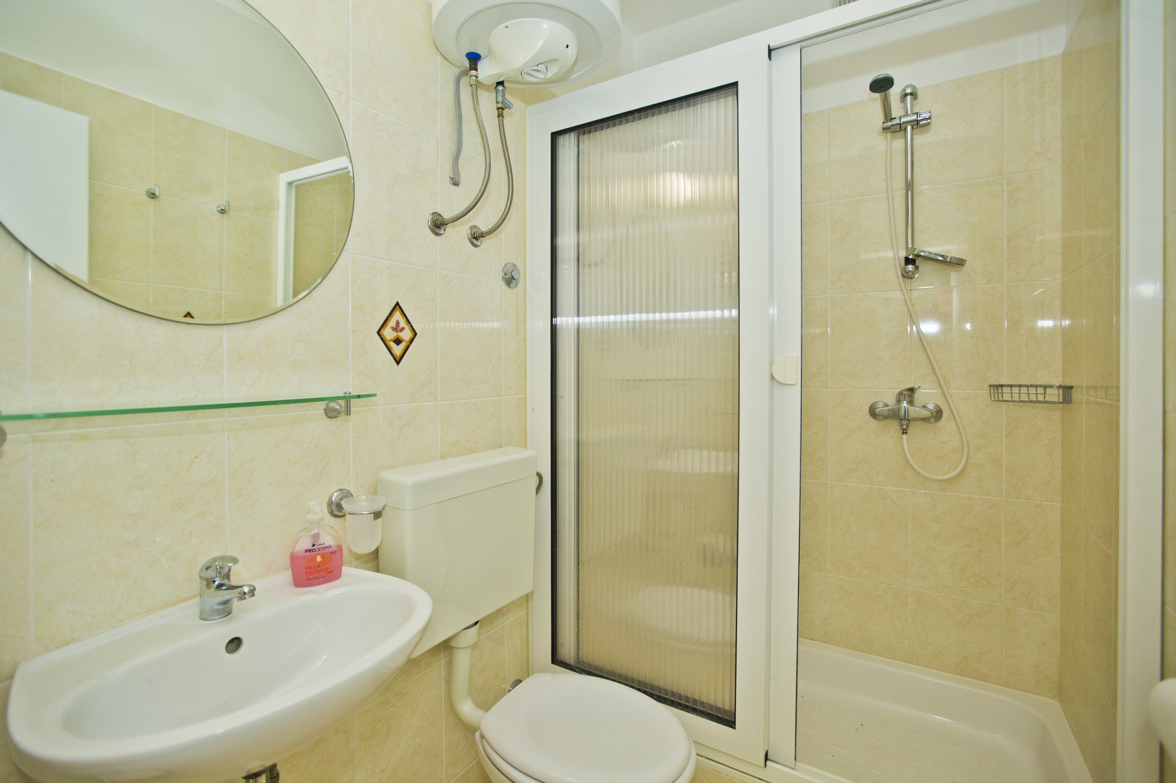 Une salle de bain équipée d’un lavabo, de toilettes, d’un miroir, d’une douche et d’une étagère en verre.