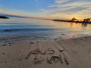 A beach with footprints and the word "SUS" and "de VOLI" written in the sand.