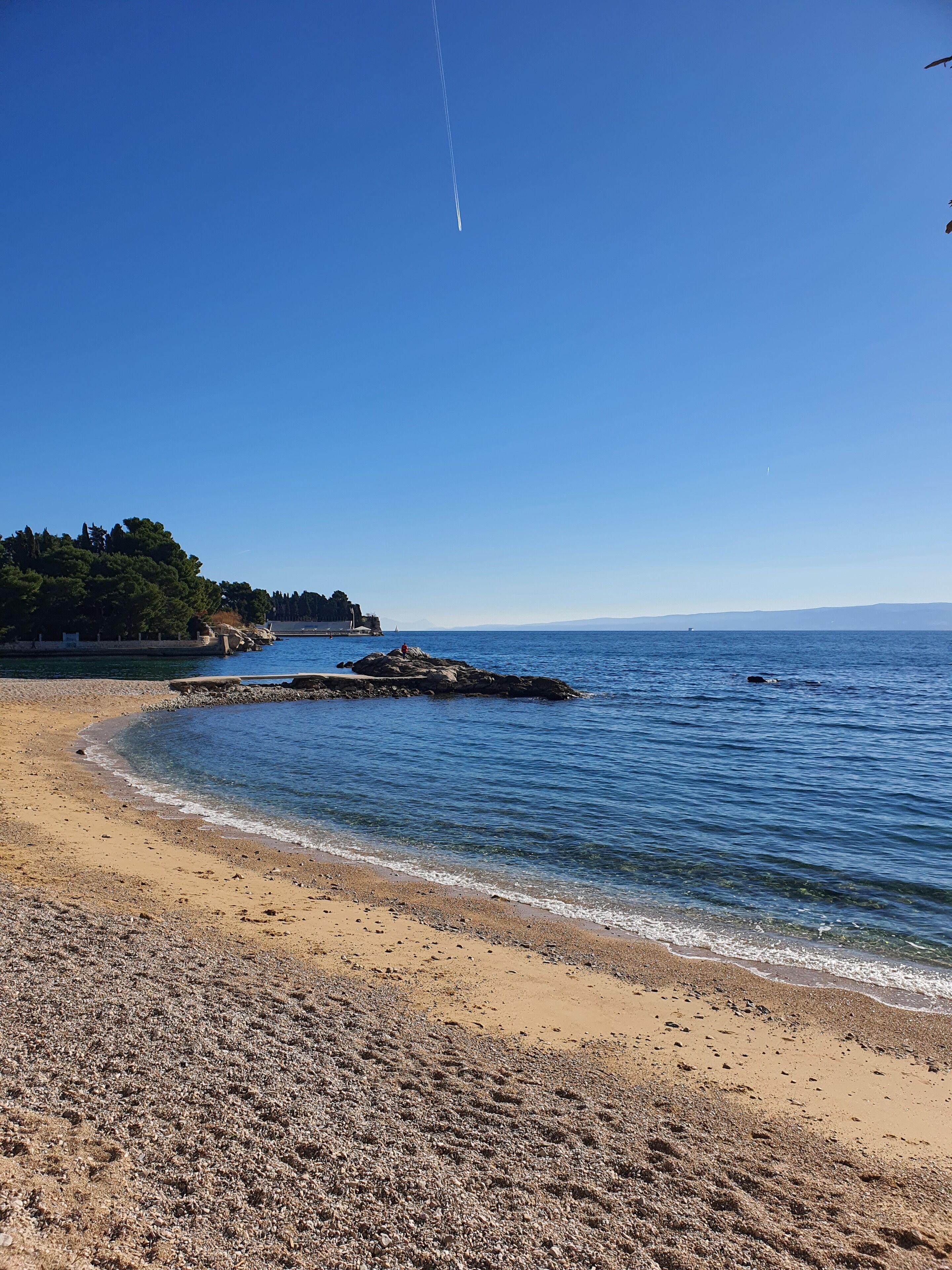 A beach with clear skies, calm waters, and rocky outcrops.