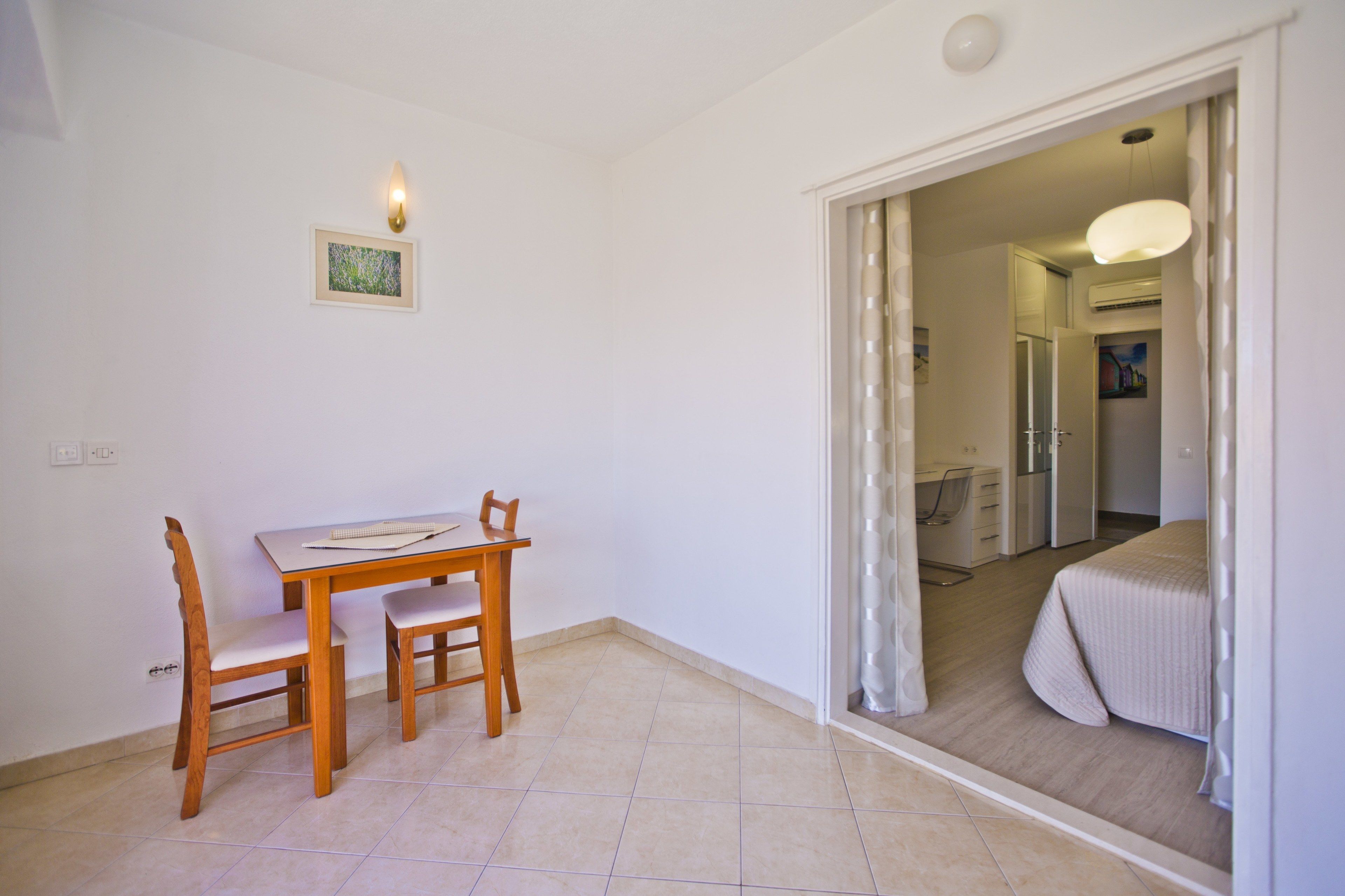 A room with a dining table and chairs, a bed with a headboard, and a doorway leading to a bathroom.