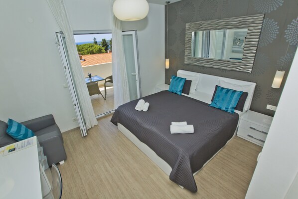 A modern hotel room with a large bed, a small desk, and a balcony with a view.