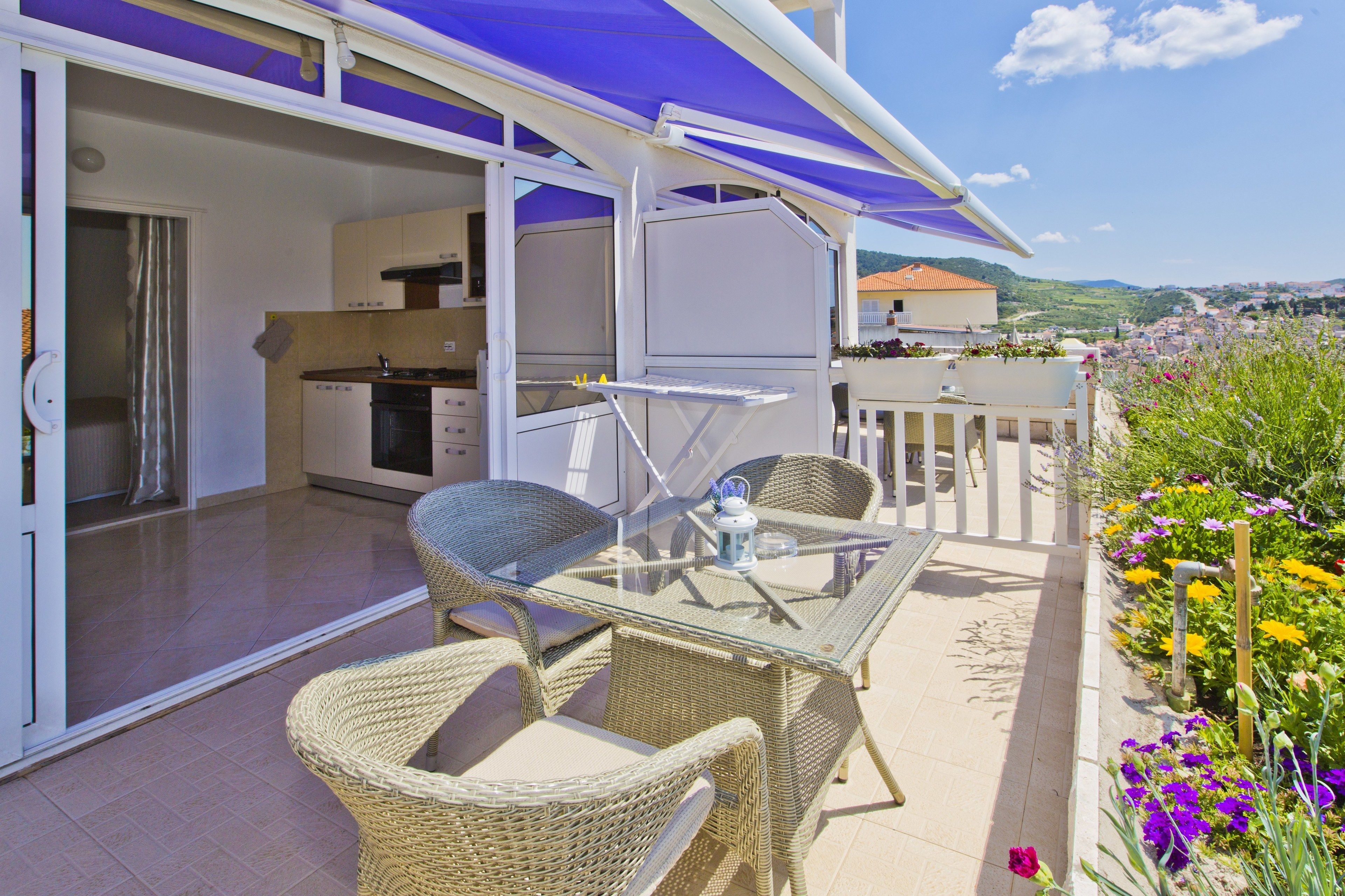 A balcony with wicker furniture, a glass table, and a view of the city.