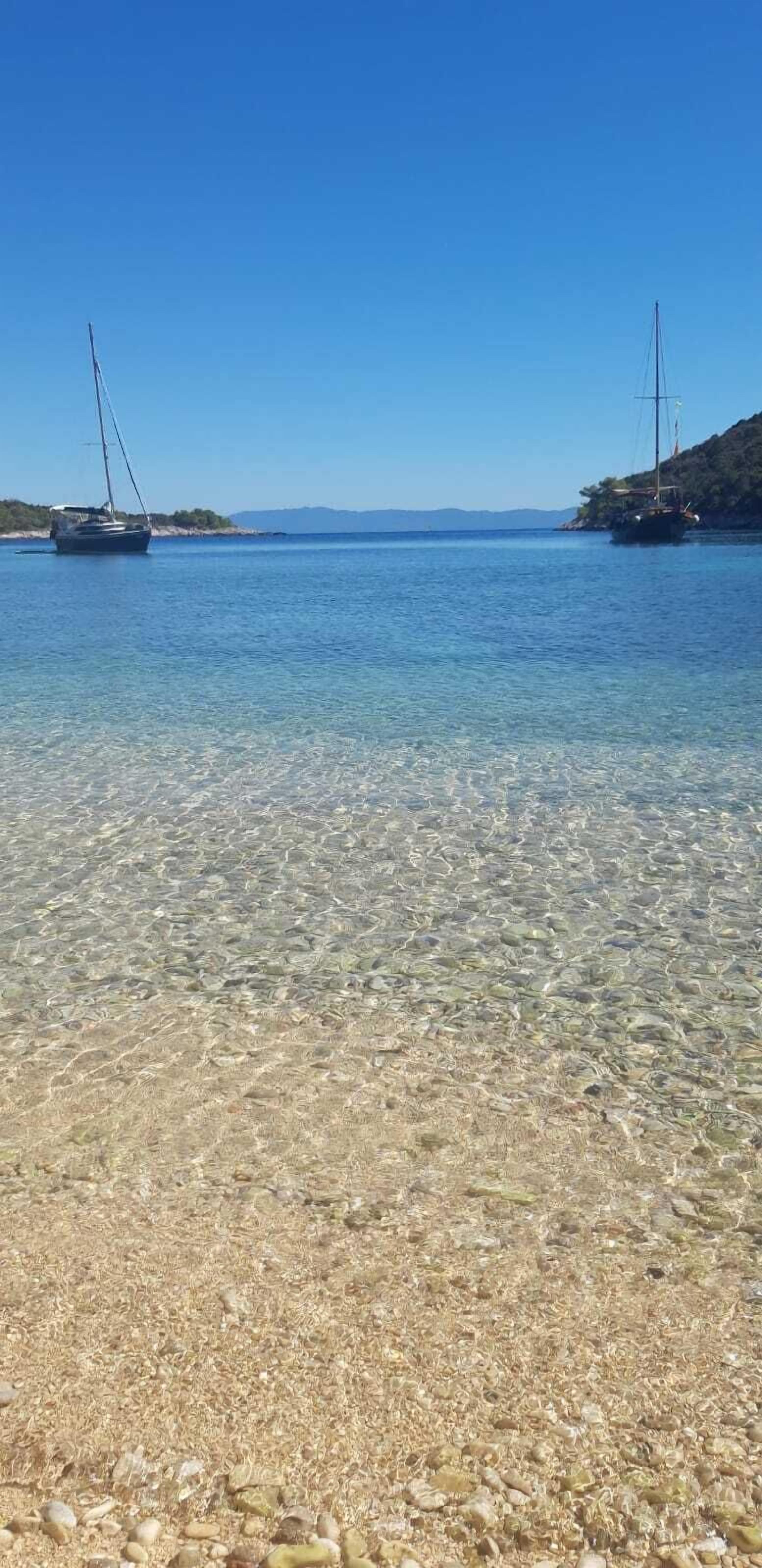 A clear shallow water body with boats and a rocky shore.