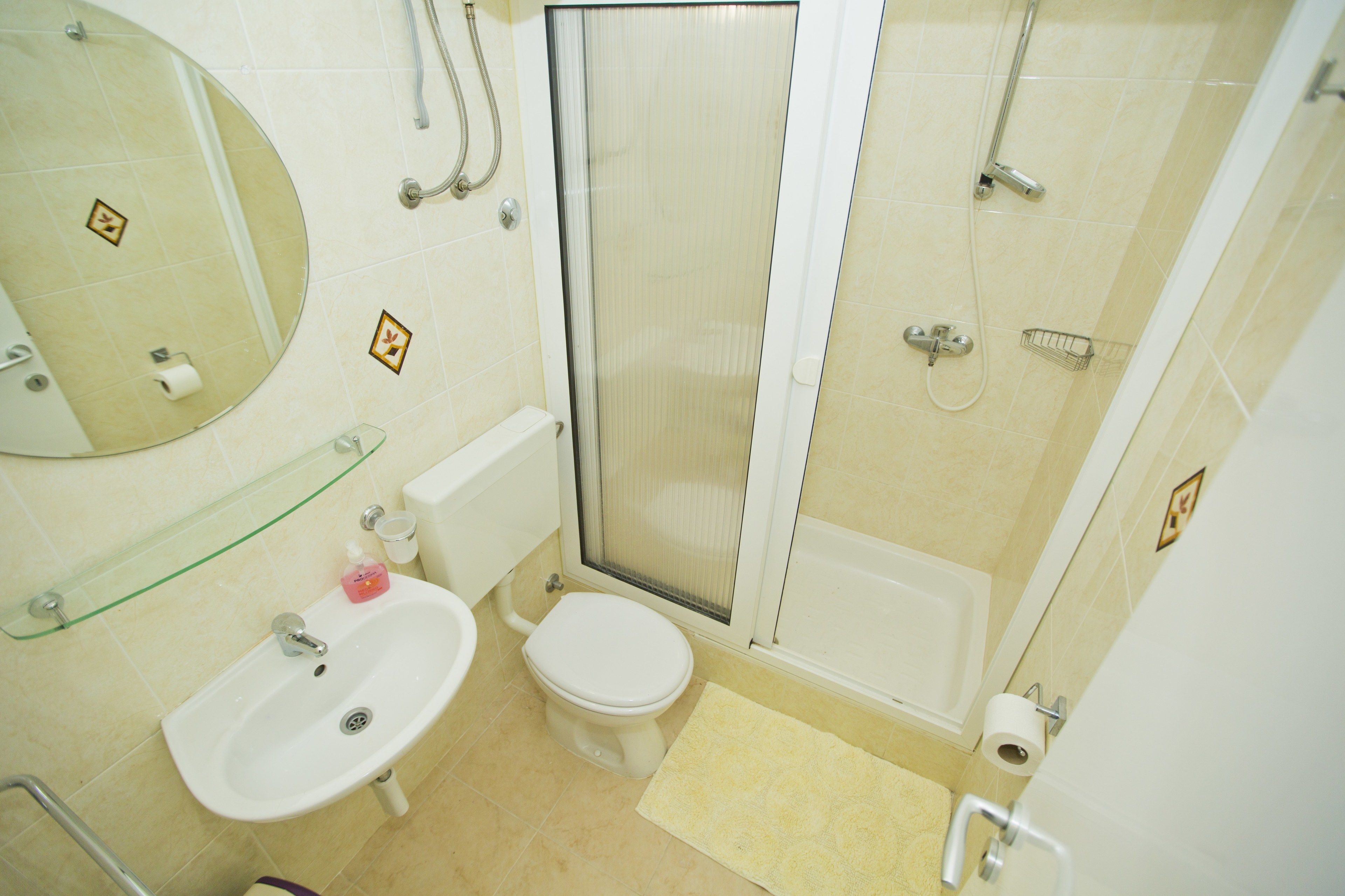 Baño con inodoro, lavabo, ducha y repisa de vidrio.