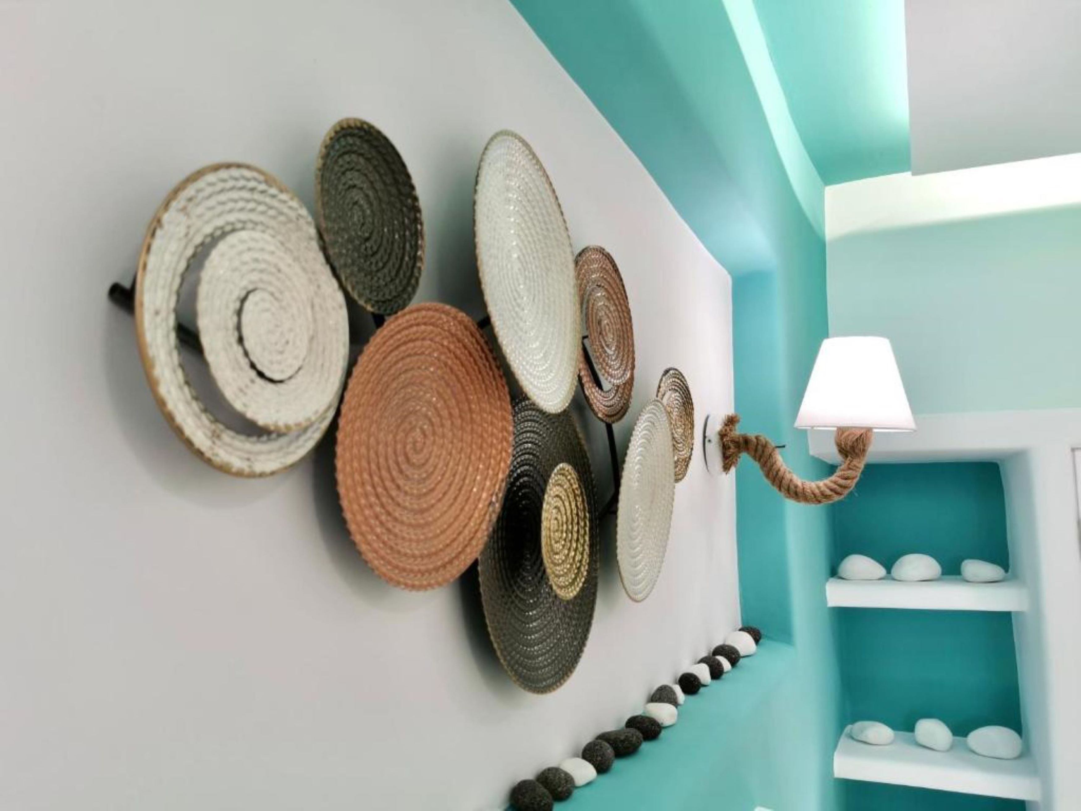 Eine Wand mit gewebten Körben unterschiedlicher Größe und Farbe, einer Lampe und Regalen mit Dekoartikeln.