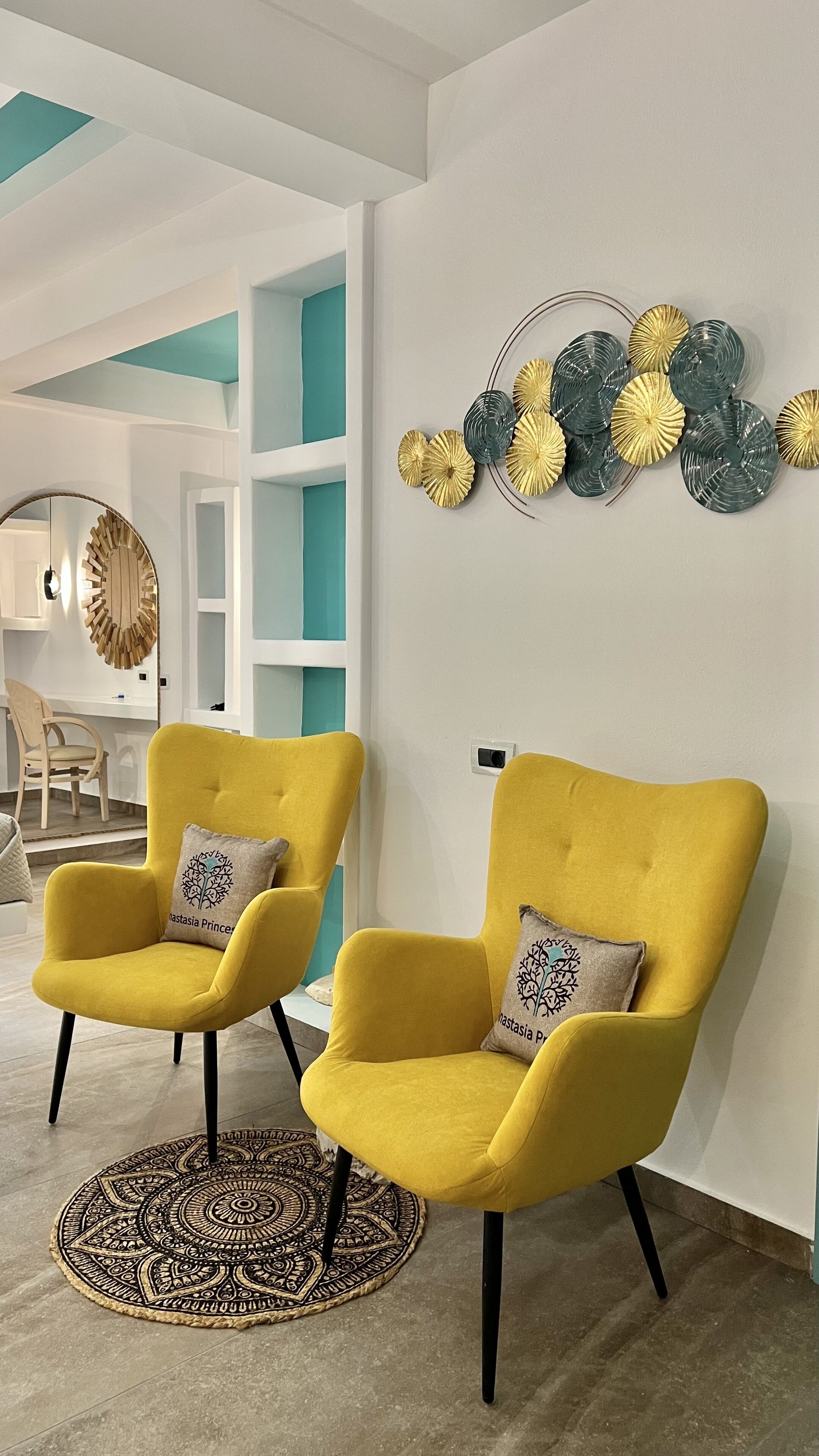 Two yellow armchairs with black legs and patterned cushions, a decorative wall piece, and a patterned rug.