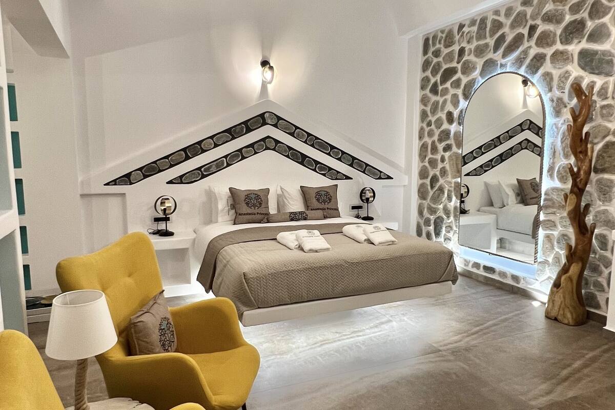 Ruime kamer met een groot bed, een accentmuur van steen en een moderne kroonluchter.