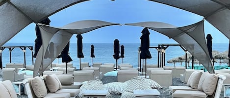 Een terras aan het strand met buitenmeubels en parasols, met uitzicht op zee.