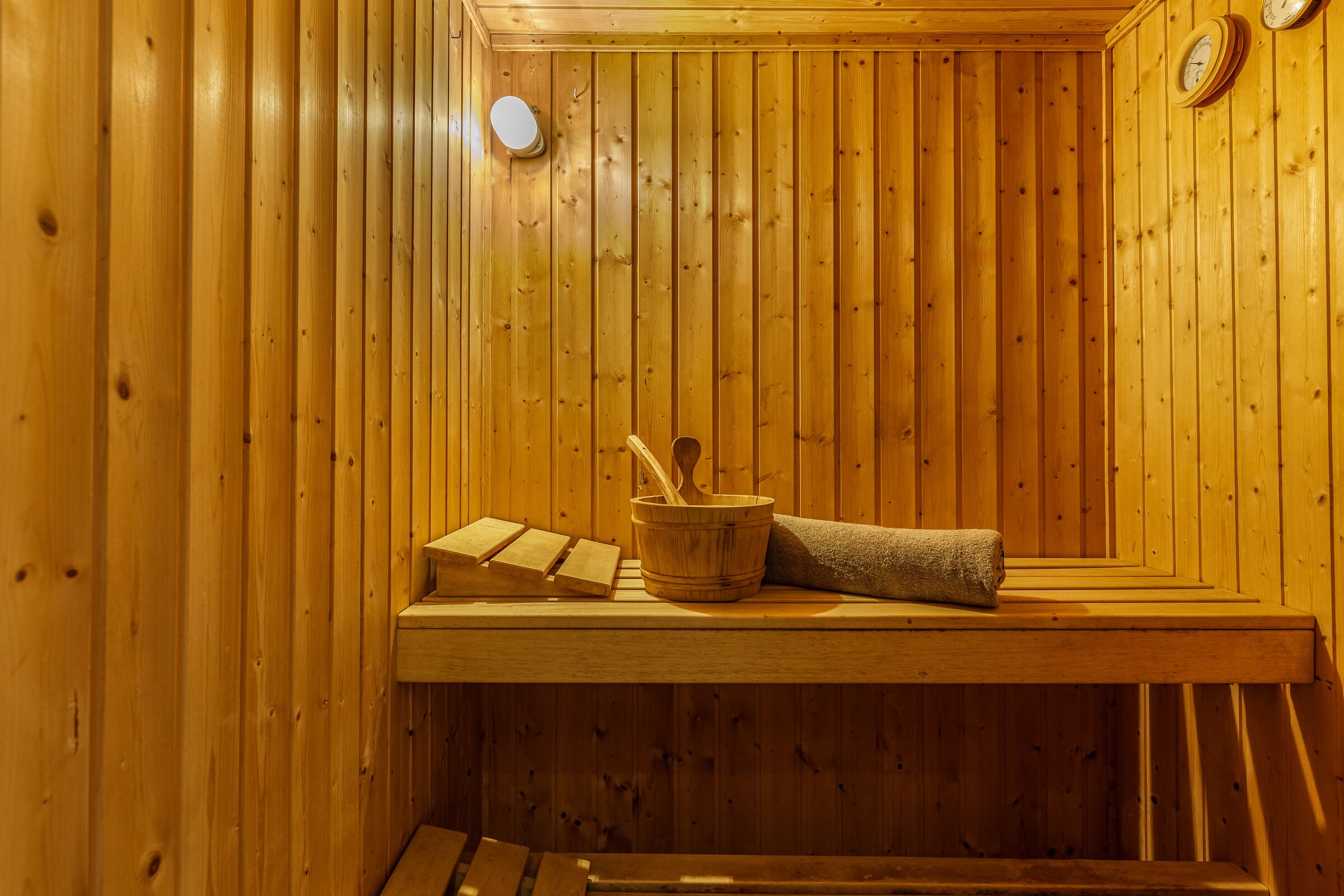 A wooden sauna with a bench, a wooden bucket, and a towel.