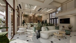 Un vestíbulo espacioso con techo alto, tragaluces, una zona de estar central con sofá y sillones, un área de bar con estantes, y un televisor grande montado en la pared.