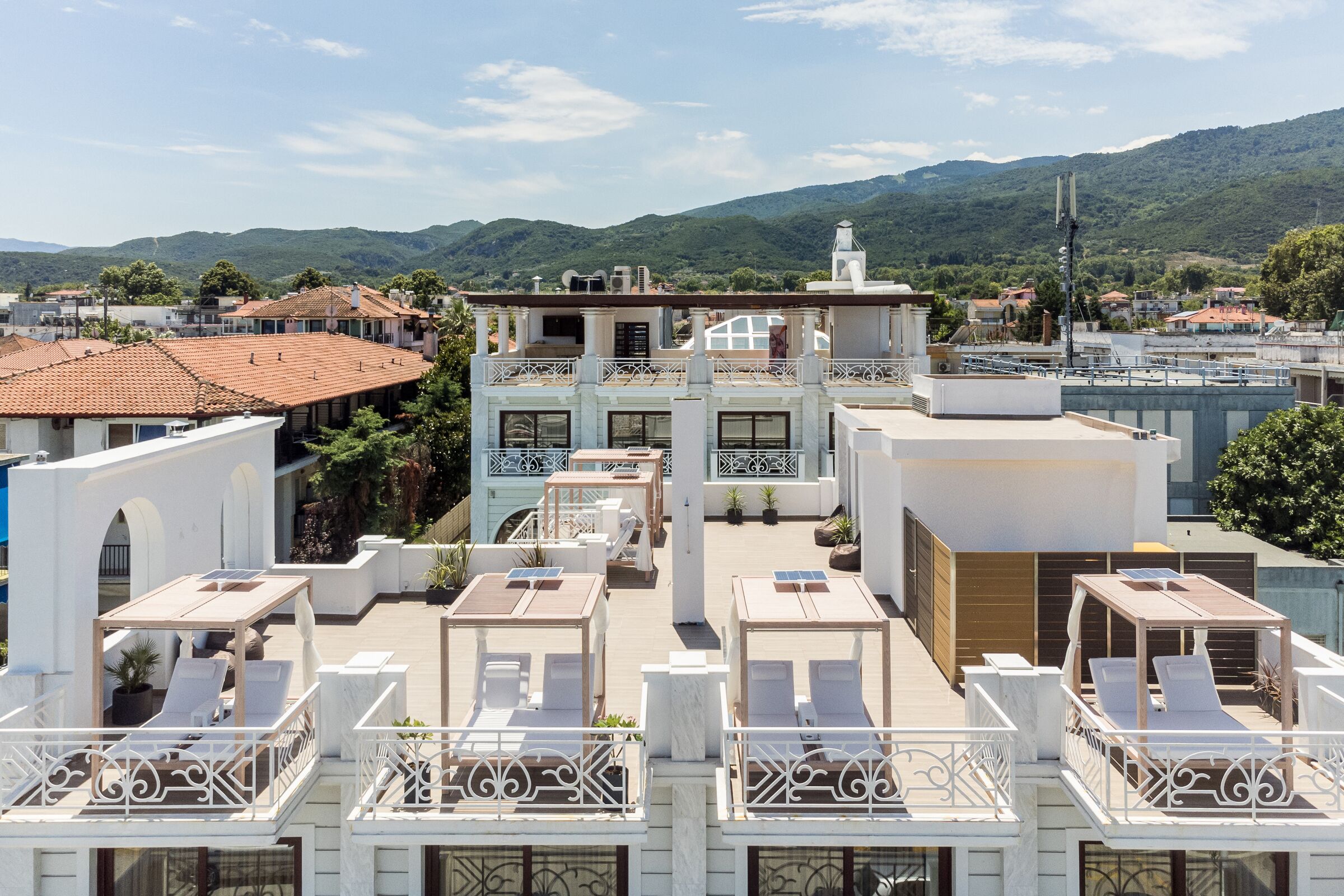 A multi-story building with a rooftop terrace featuring sun loungers and a pool.