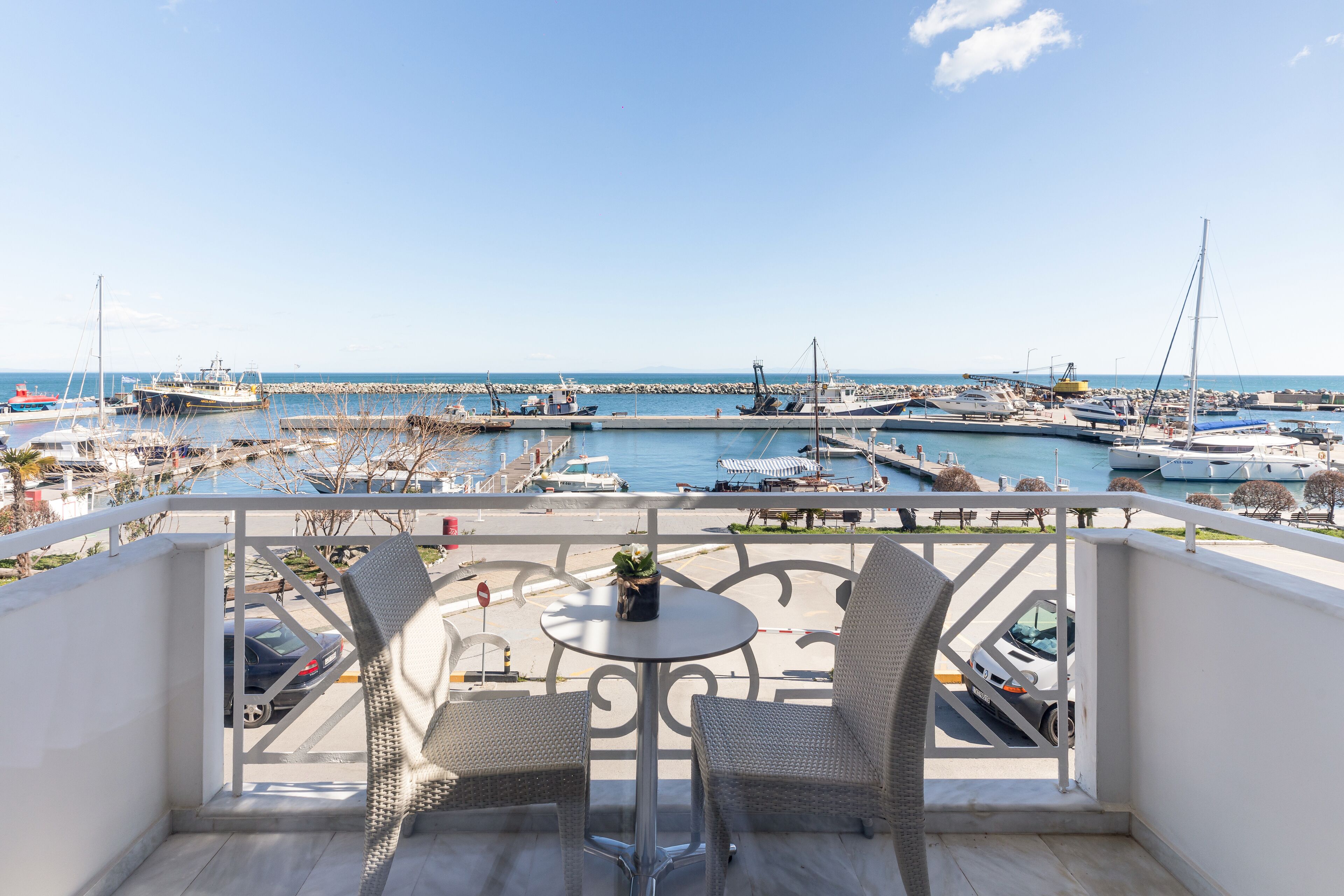 A balcony with wicker chairs and a small table, overlooking a marina with boats and a clear sky.