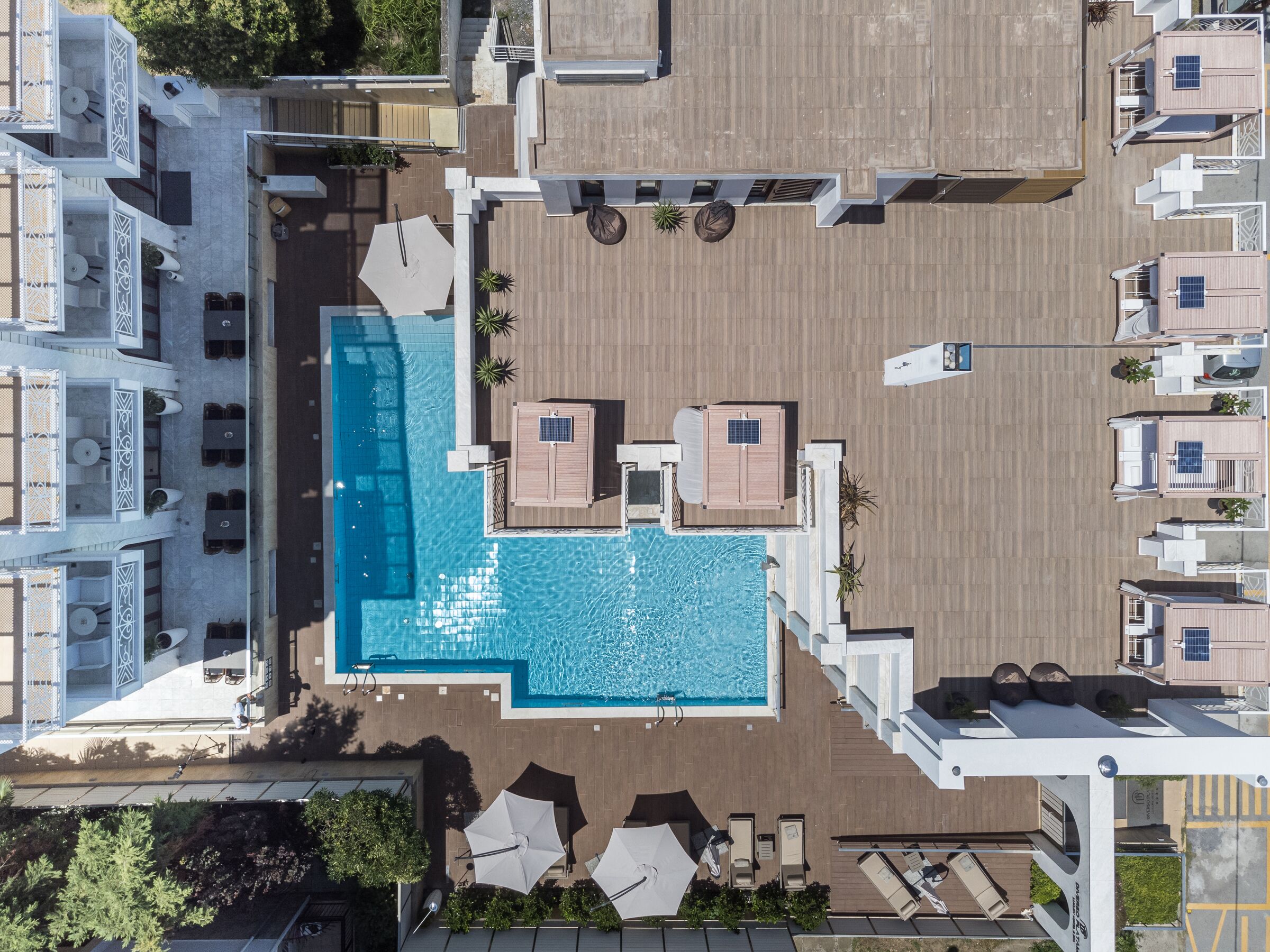 An aerial view of a hotel with a central swimming pool, multiple lounge areas, and a rooftop deck.