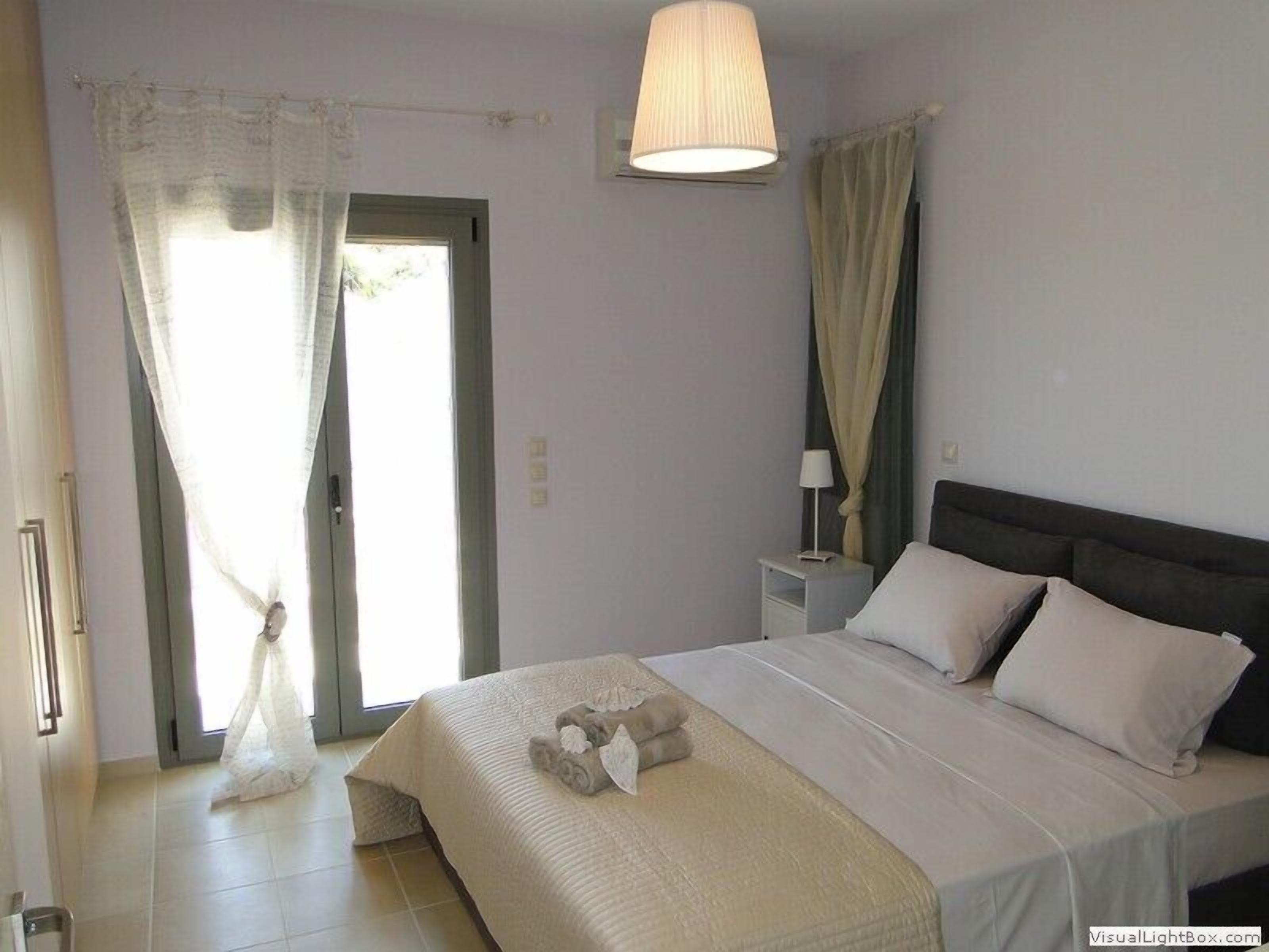 A bedroom with a bed, curtains, a nightstand, and a lamp.