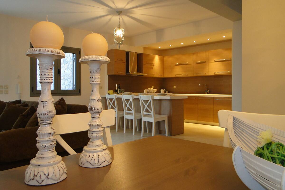 A modern kitchen with wooden cabinets, a dining area with a table and chairs, and a chandelier.