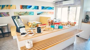 Un espace d’accueil avec un comptoir où sont exposés divers produits alimentaires, un coin salon avec une chaise, et des œuvres d’art accrochées au mur.