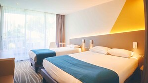Une chambre d’hôtel avec deux lits, un bureau et une grande fenêtre avec des rideaux.
