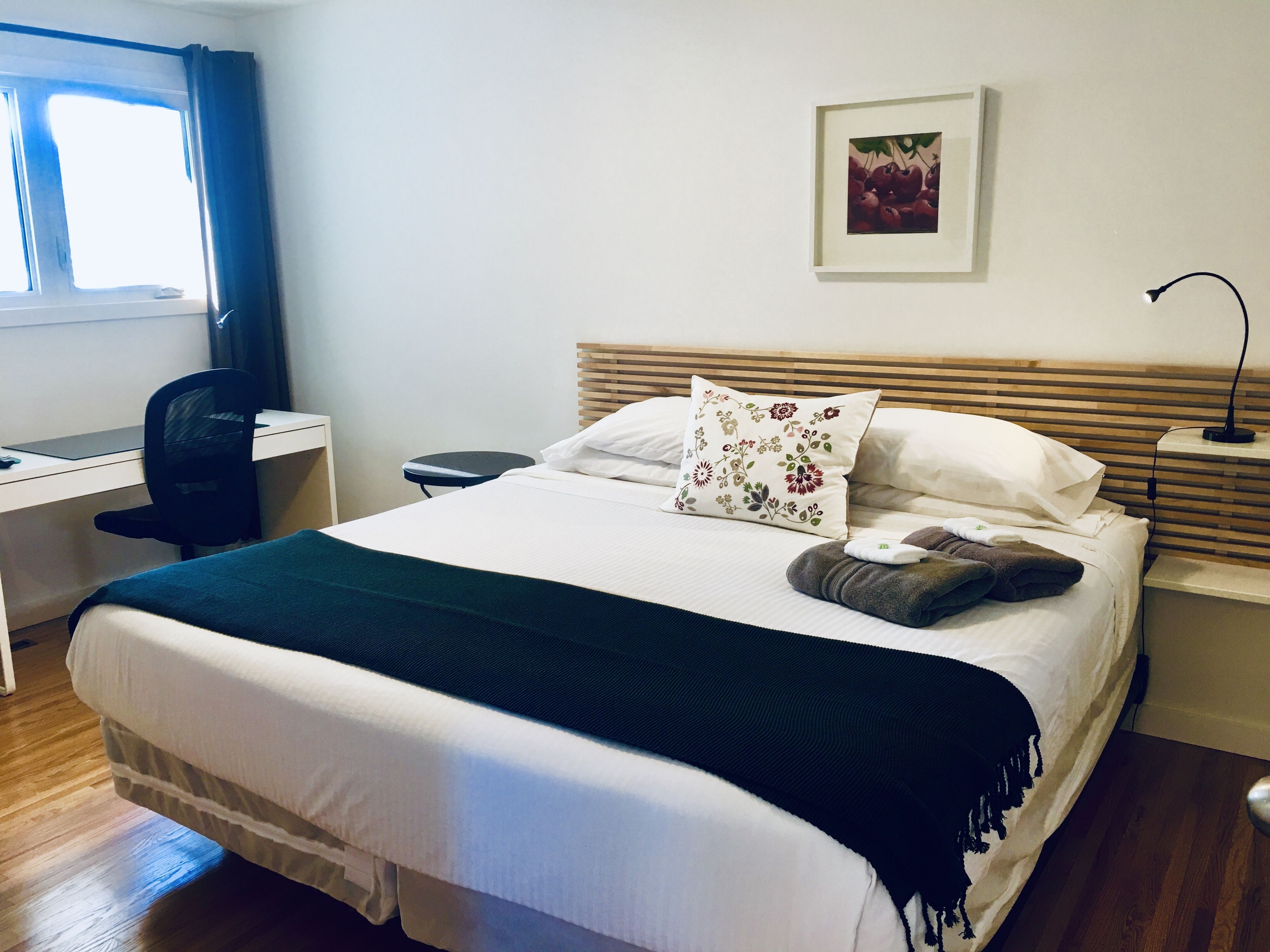 Una cama bien hecha con un cojín floral, una lámpara de noche y un escritorio con una silla.