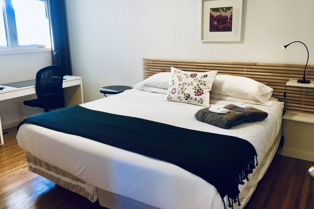 A neatly made bed with a floral pillow, a bedside lamp, and a desk with a chair.
