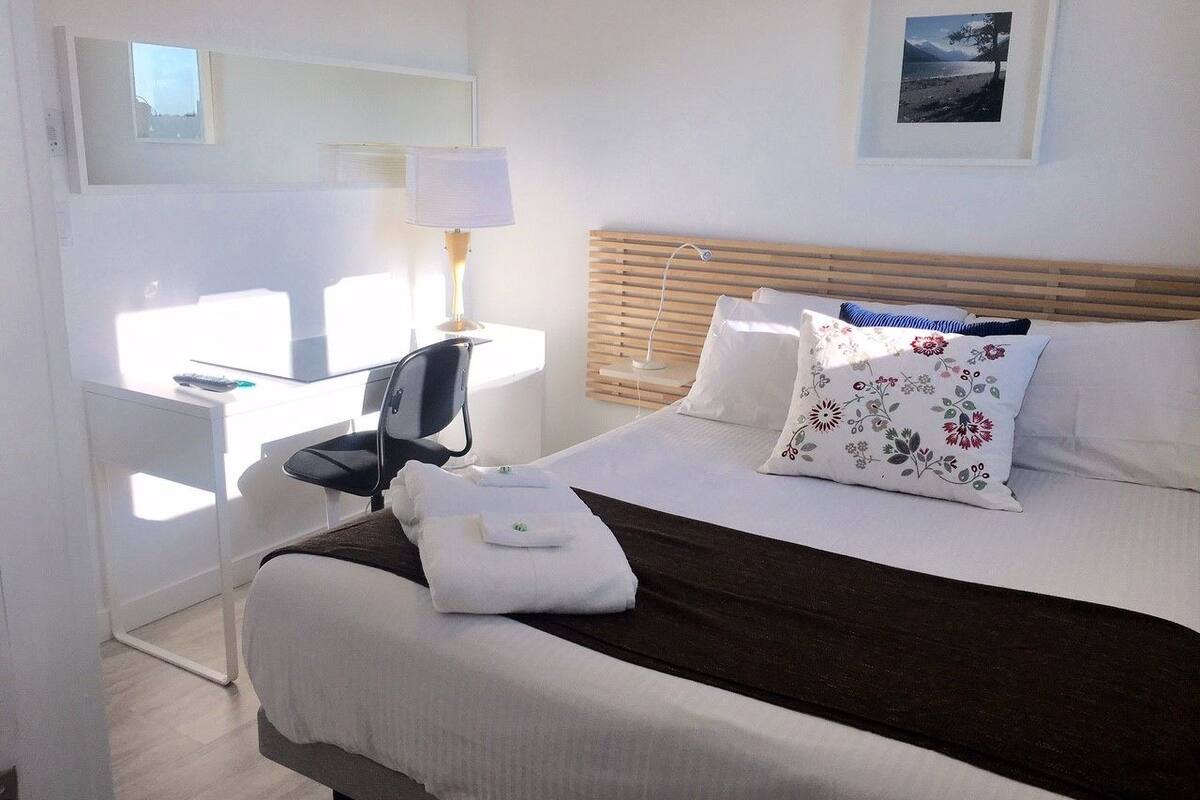 A hotel room with a bed, a desk, a chair, and a lamp.