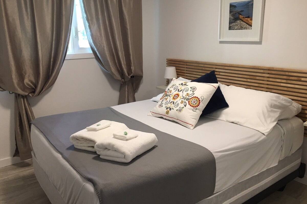 A neatly made bed with a pillow, a folded towel, and a framed picture on the wall.