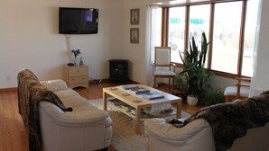 Una sala de estar con sofá, sillón, mesa de centro, televisor y ventanas amplias.