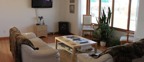 A living room with a sofa, armchair, coffee table, TV, and large windows.