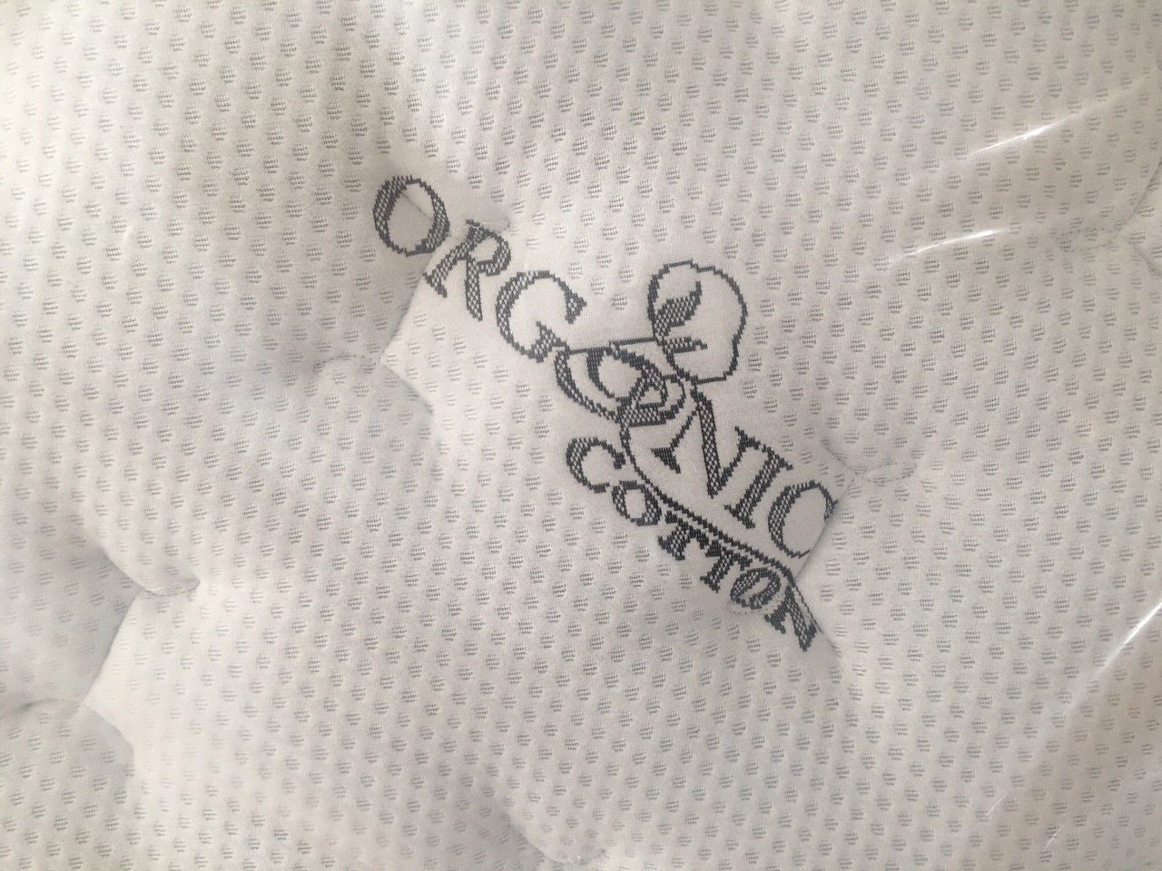 Tejido blanco de algodón orgánico con un pequeño estampado repetitivo y la inscripción 'ORGANIC COTTON' bordada.