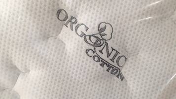 Tejido blanco de algodón orgánico con un pequeño estampado repetitivo y la inscripción 'ORGANIC COTTON' bordada.