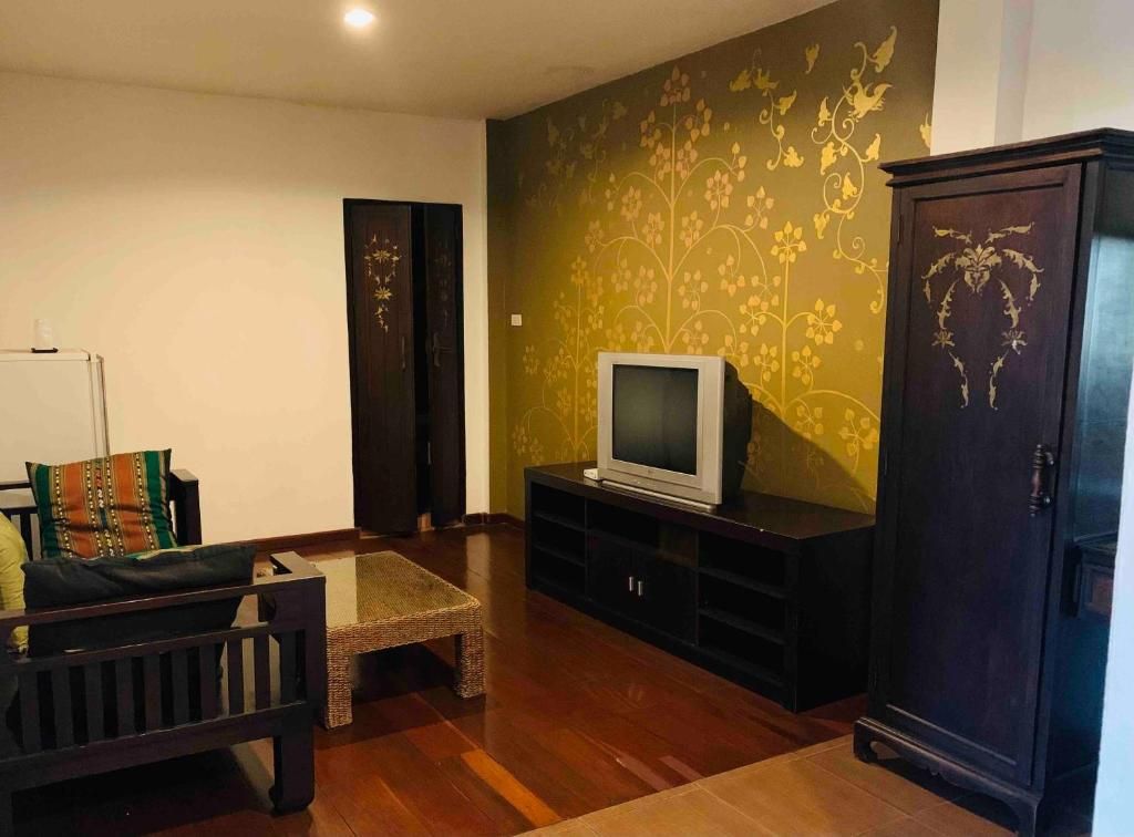A living room with a television on a stand, a dark wooden cabinet, and a patterned wall.