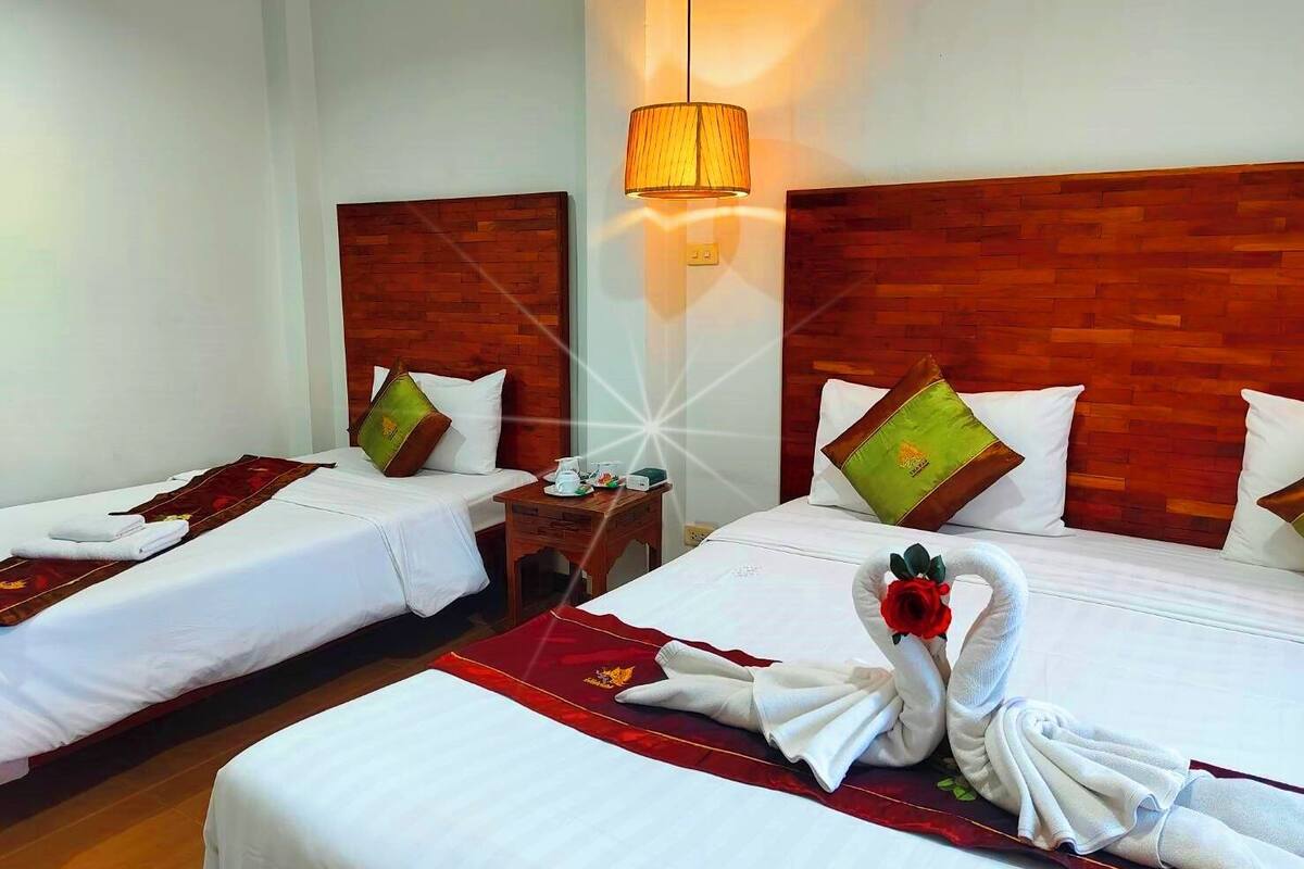 Une chambre d’hôtel avec deux lits, des têtes de lit en bois, un plaid rouge et une lampe fixée au mur.