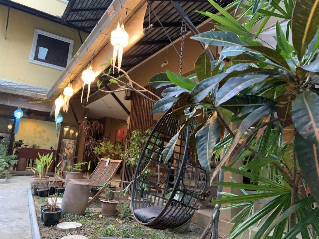 A hanging chair in a garden area with potted plants and a building in the background.
