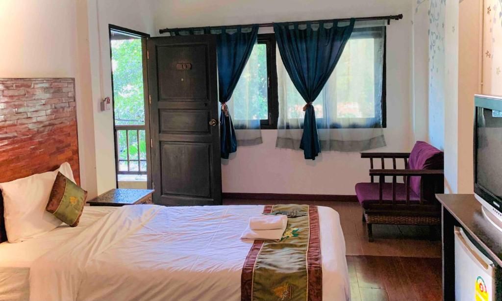 A hotel room with a bed, a TV, a window with curtains, a wooden headboard, and a small table.