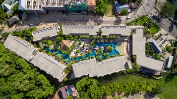 Vista aérea de un hotel con piscina central rodeada de abundante vegetación y varios edificios.