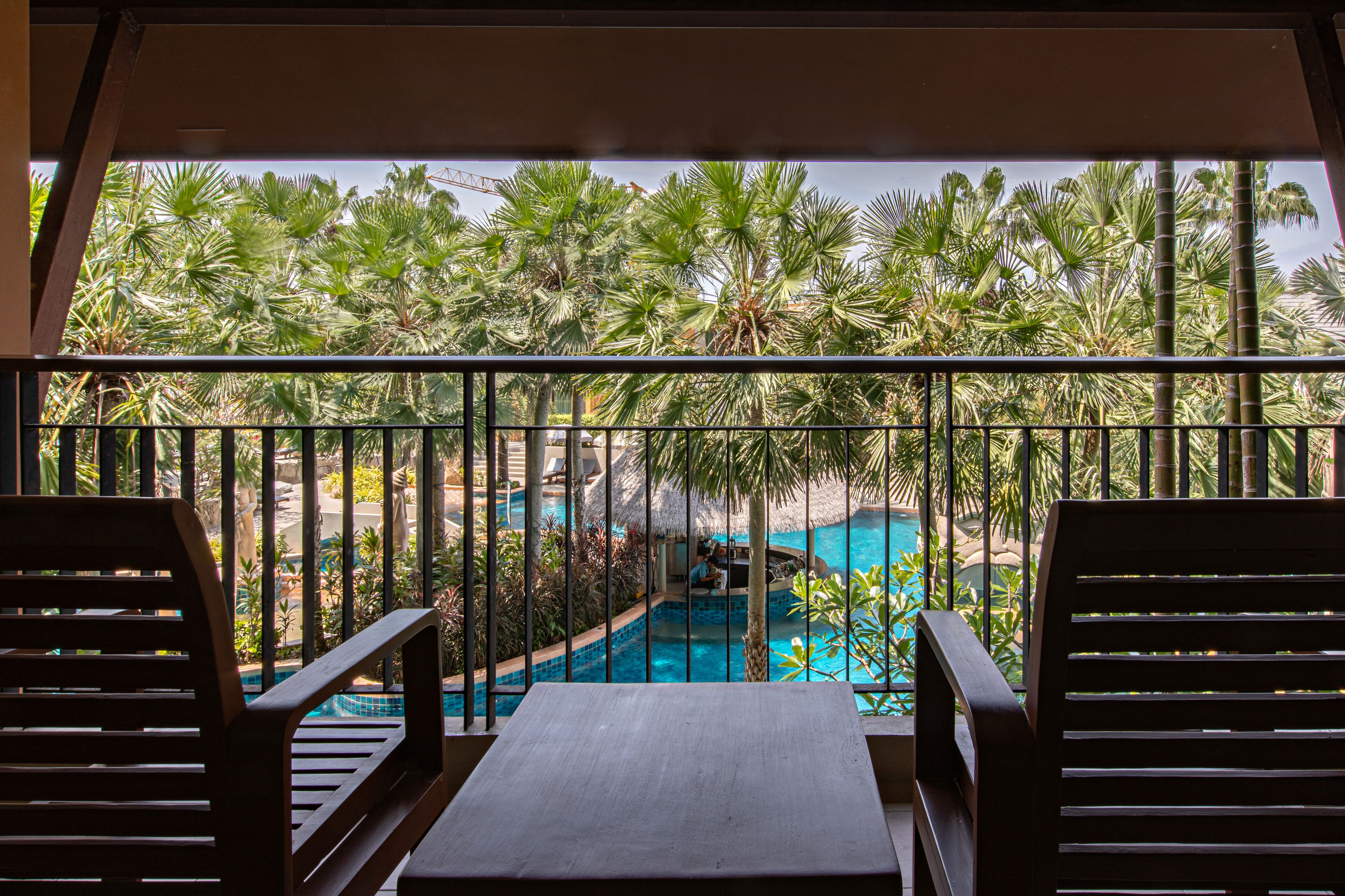 A balcony with a view of a swimming pool surrounded by palm trees.