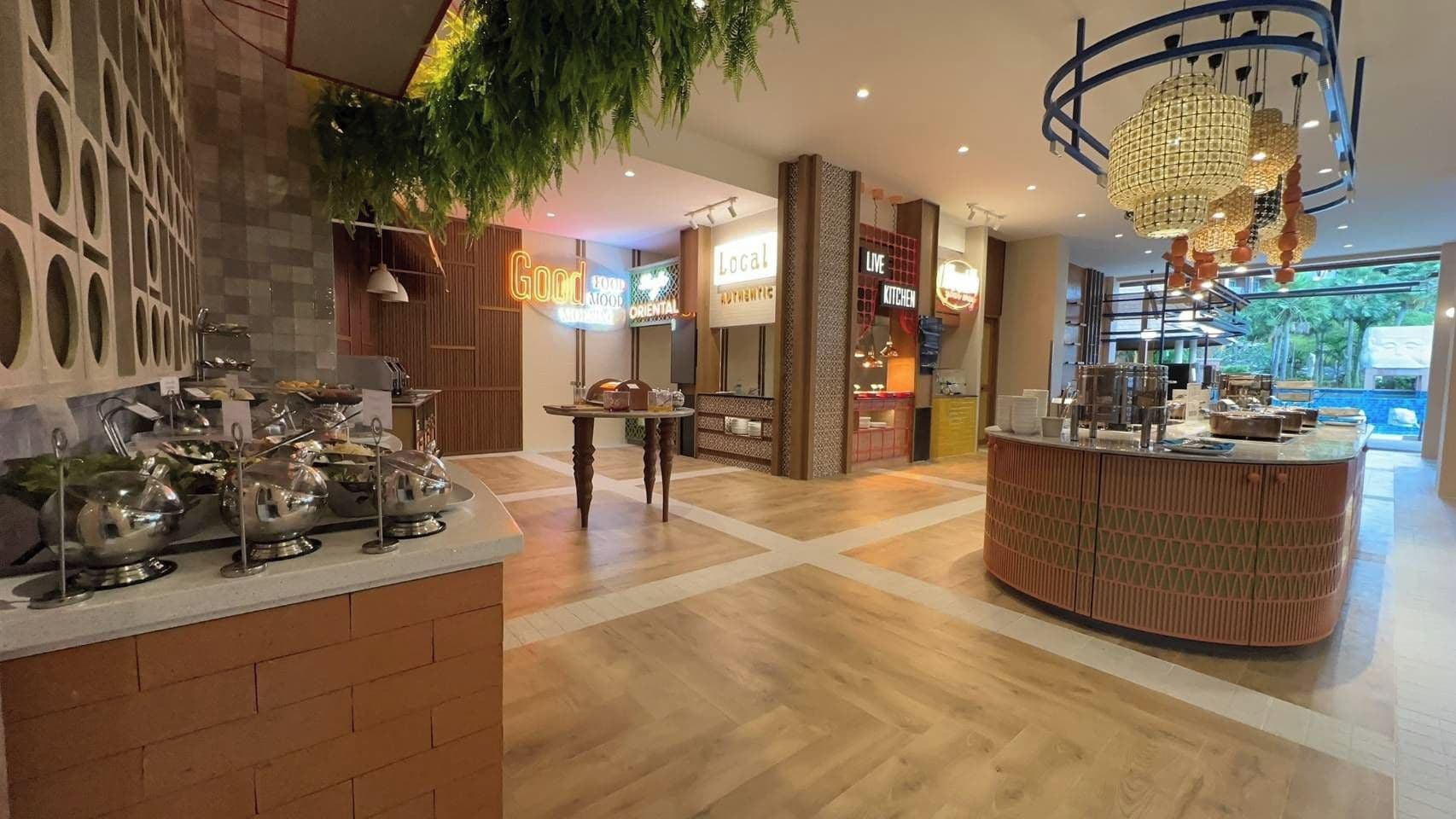 A modern restaurant interior with a central dining area, a bar, and a kitchen visible in the background.