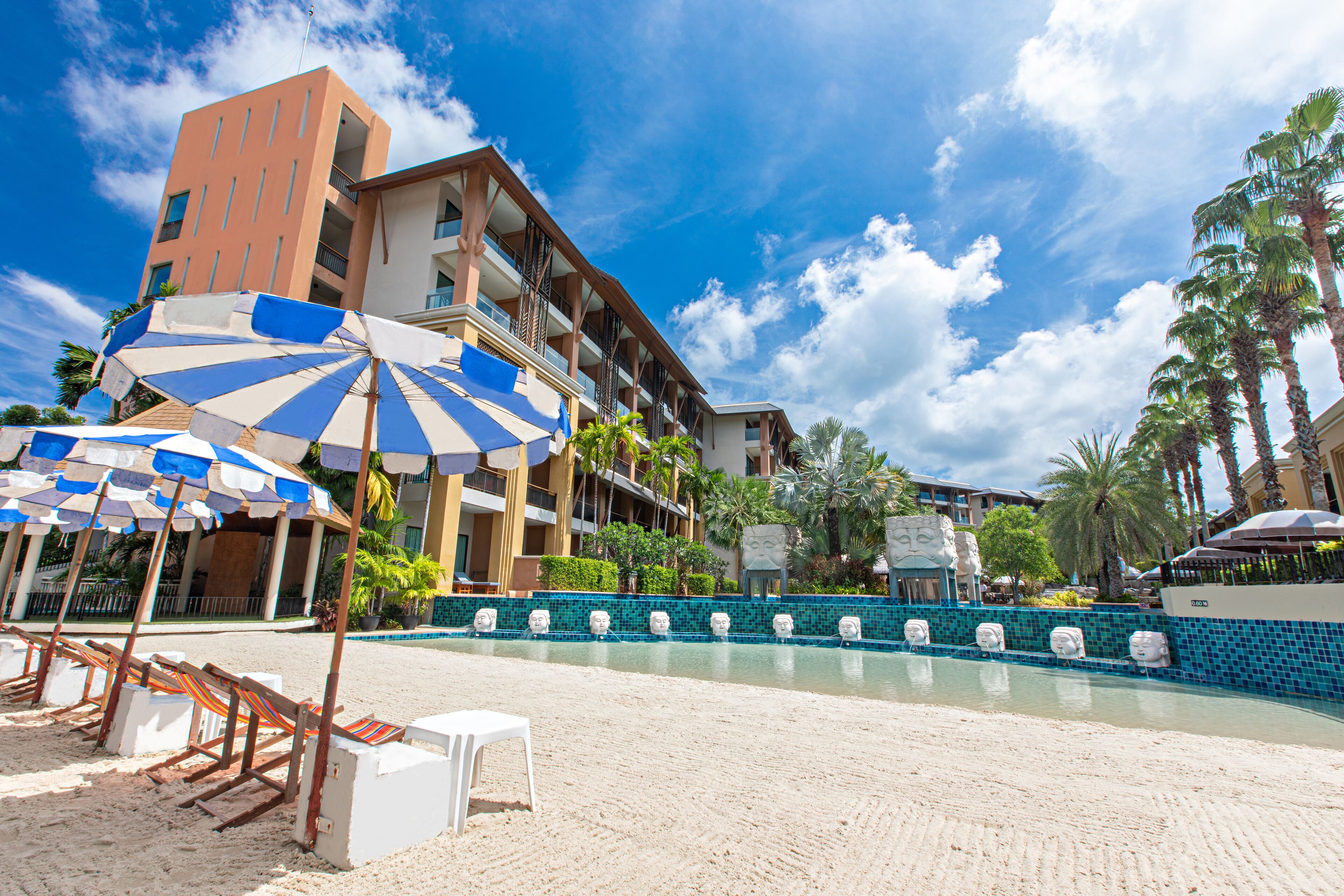 A beachside hotel with a pool, umbrellas, and lounge chairs.