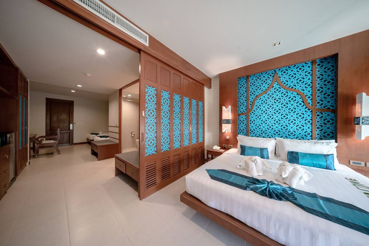 A modern hotel room with a large bed, a wooden wardrobe, a seating area, and a bathroom.
